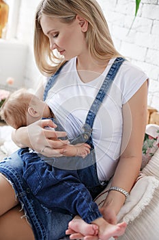 Young mother breastfeeding a child sitting on a bed in a bright bedroom