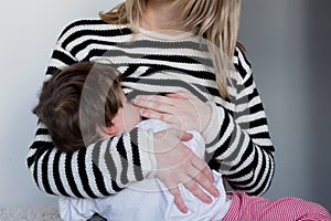 Young mother breastfeeding toddler boy in striped sweater