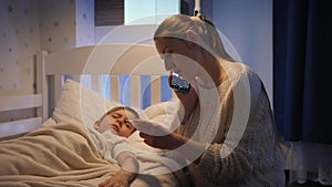 Young mother calling doctor or 911 emergency to her sick little son lying in bed. Concept of children illness, disease