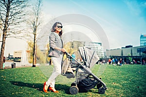 Young mother carrying child in pram. Mother walking in park with newborn and pram