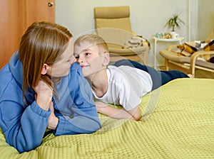 Young mother in casual clothes lies on the bed next to her son, having fun together in a cozy bedroom at home. Happy children with