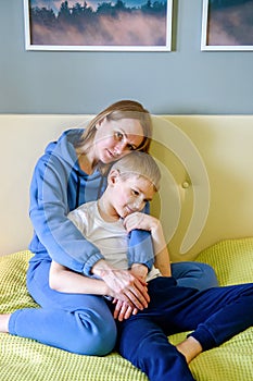 Young mother in casual clothes lies on the bed next to her son, having fun together in a cozy bedroom at home. Happy children with