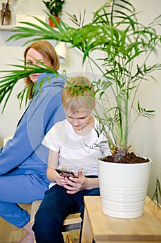 Young mother in casual clothes next to her son, looking through information on the phone. Happy kids with Mom