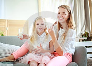 Young mother with child daughter at home on couch drinking milk and cookies, laughing and talking together