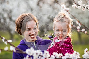 Young mother and child daughter together, hugging and laughing in a Flowering apricot garden. Family outdoors lifestyle