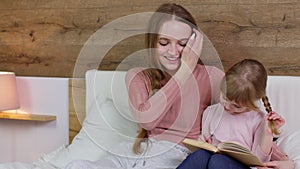 Young mother and child kid daughter lying in bed at home, reading book bedtime stories, fairytales