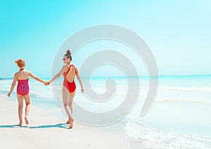 Young mother and child in red beachwear on seacoast walking