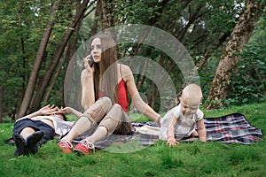 Young mother with child sitting on picnic blanket and talking on phone. Business woman with baby