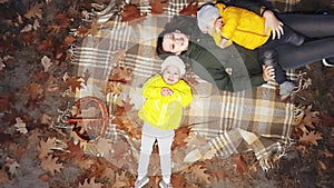 A young mother with children lies on a plaid in an autumn park and catches falling leaves.