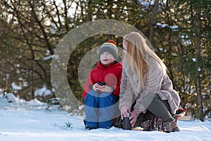 Young mother and children son in winter forest. Family trip out of town. Picnic in the snowy forest