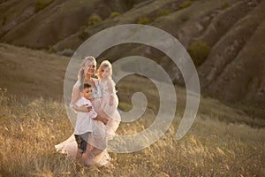 A young mother with children walks in a field at sunset. Country style