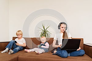 Young mother with computer in hand and kids with phones sitting on couch. Overuse of devices