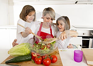 Young mother in cook apron and sweet beautiful twin daughters cooking preparing together salad