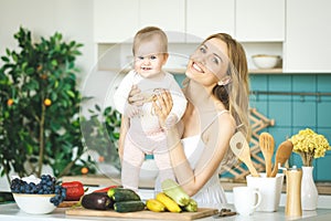 Young mother is cooking and playing with her baby daughter in a kitchen setting. Healthy food concept