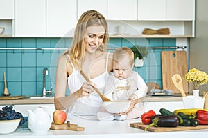 Young mother is cooking and playing with her baby daughter in a kitchen setting. Healthy food concept