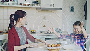 Young mother and cute daughter cooking together talking in the kitchen on weekend. Little girl clapping hands with flour