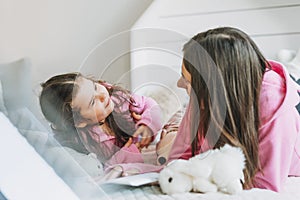 Young mother and cute girl in pink family looks hoodie on bed in children room, bright scandinavian interior, birthday, christmas