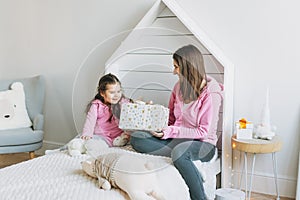 Young mother and cute girl in pink family looks hoodie on bed in children room, bright scandinavian interior, christmas time