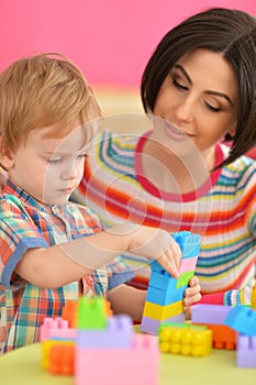 Young mother and cute little son playing with colorful plastic blocks