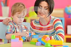 Young mother and cute little son playing with colorful plastic blocks