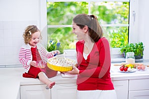 Young mother and daughter baking a pie together