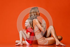 Young mother and daughter doing yoga exercises together in a fitness studio on a red background