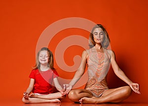 Young mother and daughter doing yoga exercises together in a fitness studio on a red background