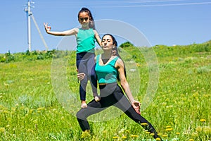 Young mother and daughter doing yoga exercises, young woman doing yoga exercises in the park, mother and daughter doing yoga