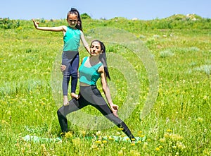 Young mother and daughter doing yoga exercises, young woman doing yoga exercises in the park, mother and daughter doing yoga