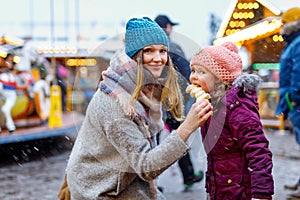 Young mother and daughter eating white chocolate covered fruits on skewer on traditional German Christmas market