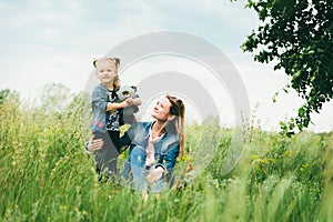 Young mother with daughter in nature among the green grass