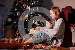 young mother and daughter open Christmas Lighting Present Gift Box front of Xmas Tree. Happy Mom with kid girl in Magic