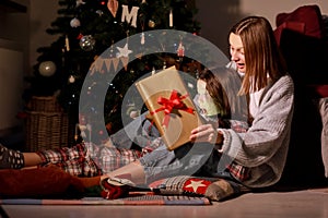 young mother and daughter open Christmas Lighting Present Gift Box front of Xmas Tree. Happy Mom with kid girl in Magic