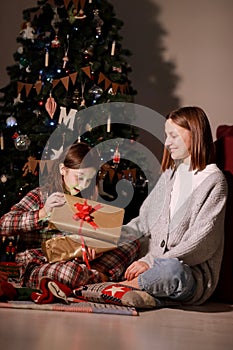 young mother and daughter open Christmas Lighting Present Gift Box front of Xmas Tree. Happy Mom with kid girl in Magic