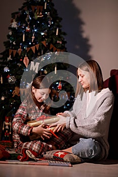 young mother and daughter open Christmas Lighting Present Gift Box front of Xmas Tree. Happy Mom with kid girl in Magic