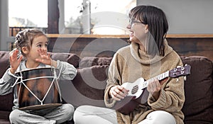 Young mother and daughter play musical instruments at home