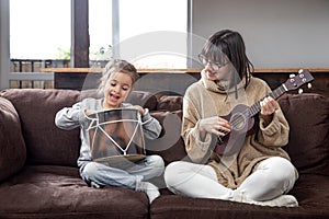 Young mother and daughter play musical instruments at home