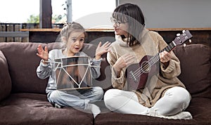 Young mother and daughter play musical instruments at home