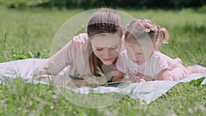 Young Mother And Daughter Reading Book Lying On Grass At Park