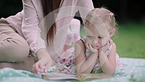 Young Mother And Daughter Reading Book Lying On Grass At Park