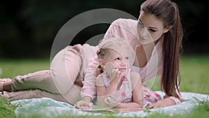 Young Mother And Daughter Reading Book Lying On Grass At Park