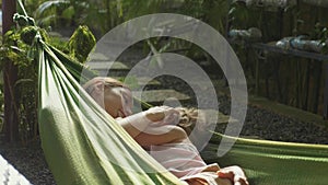 Young mother and daughter relaxing together in a hammock at garden in summer day