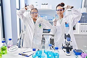 Young mother and daughter at scientist laboratory smiling making frame with hands and fingers with happy face