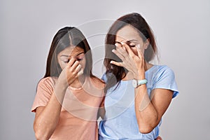 Young mother and daughter standing over white background tired rubbing nose and eyes feeling fatigue and headache