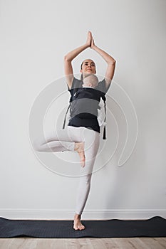 Young mother doing yoga with baby in ergo backpack