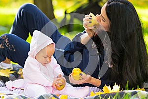 Young mother eating autumn apples with her baby.