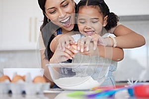 Young mother enjoying baking, bonding with her little daughter in the kitchen at home. Little latino girl smiling while photo