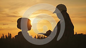 Young mother farmer teaches her daughter to work in a wheat field. Silhouette of a farmers family in a wheat field at