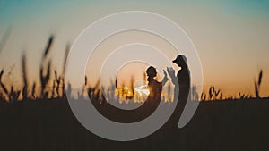 Young mother farmer teaches her daughter to work in a wheat field. Silhouette of a farmers family in a wheat field at