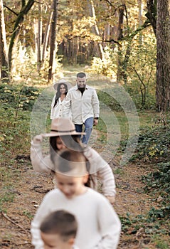 Young mother, father with daughter and sons are walking, having fun in autumn forest. Family holding hands enjoying time